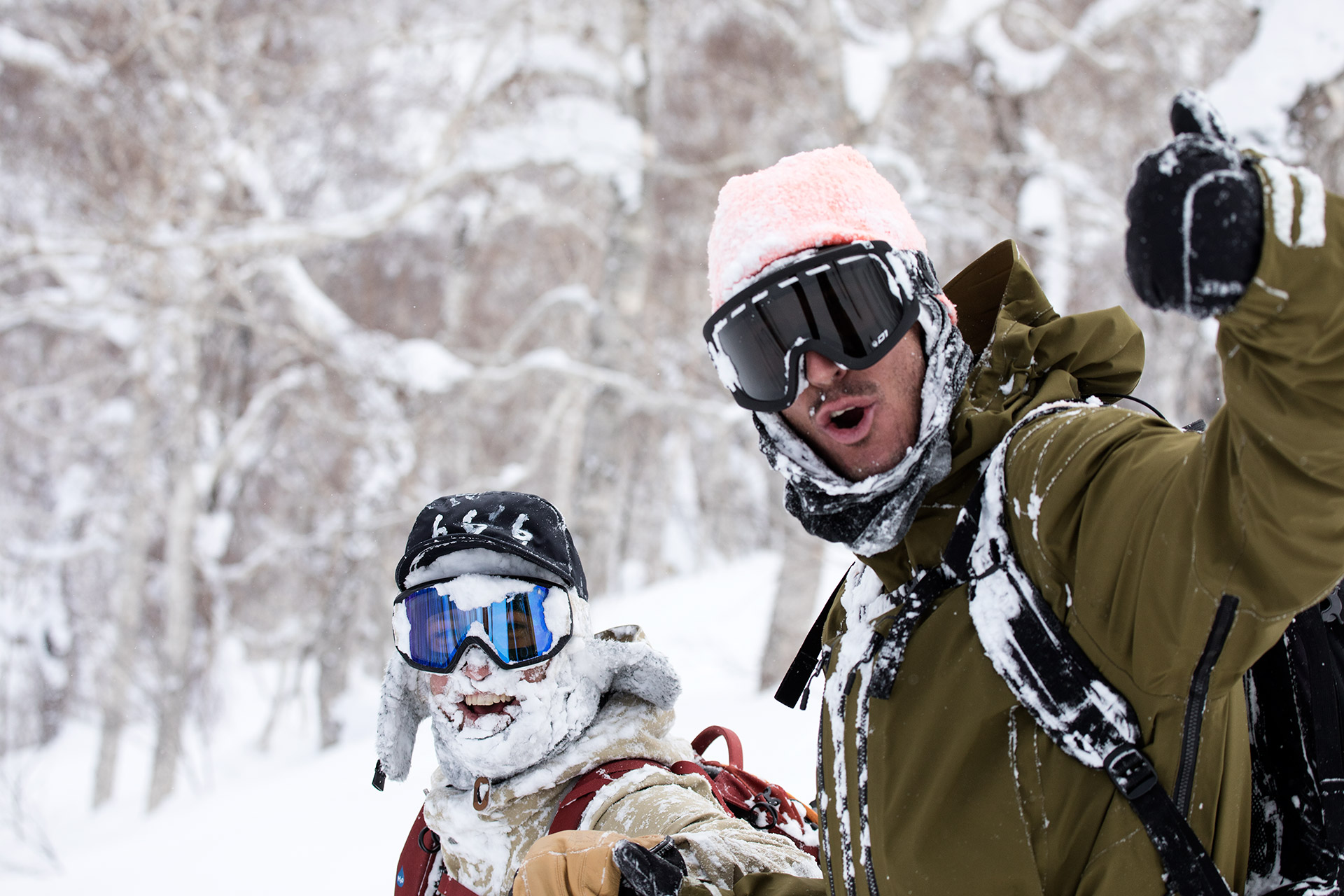Two snow-caked riders, thumbs up after a deep day
