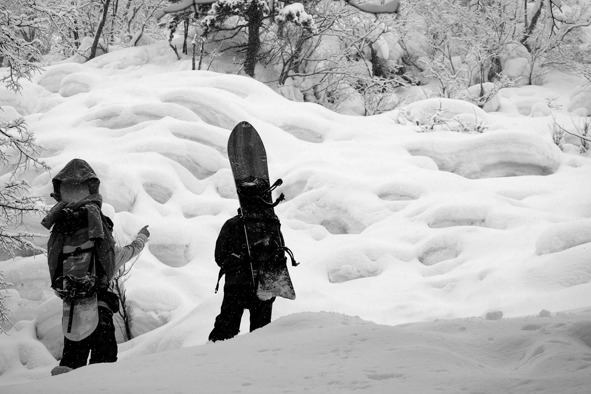 Two riders hiking through pillowed snow, boards on their backs