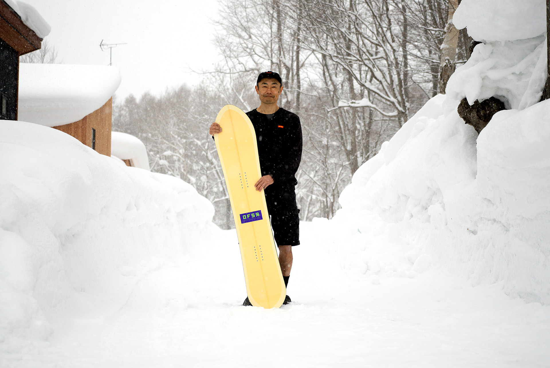 Tomohito Yamazaki holding a finished board in a snowed-in Niseko lane