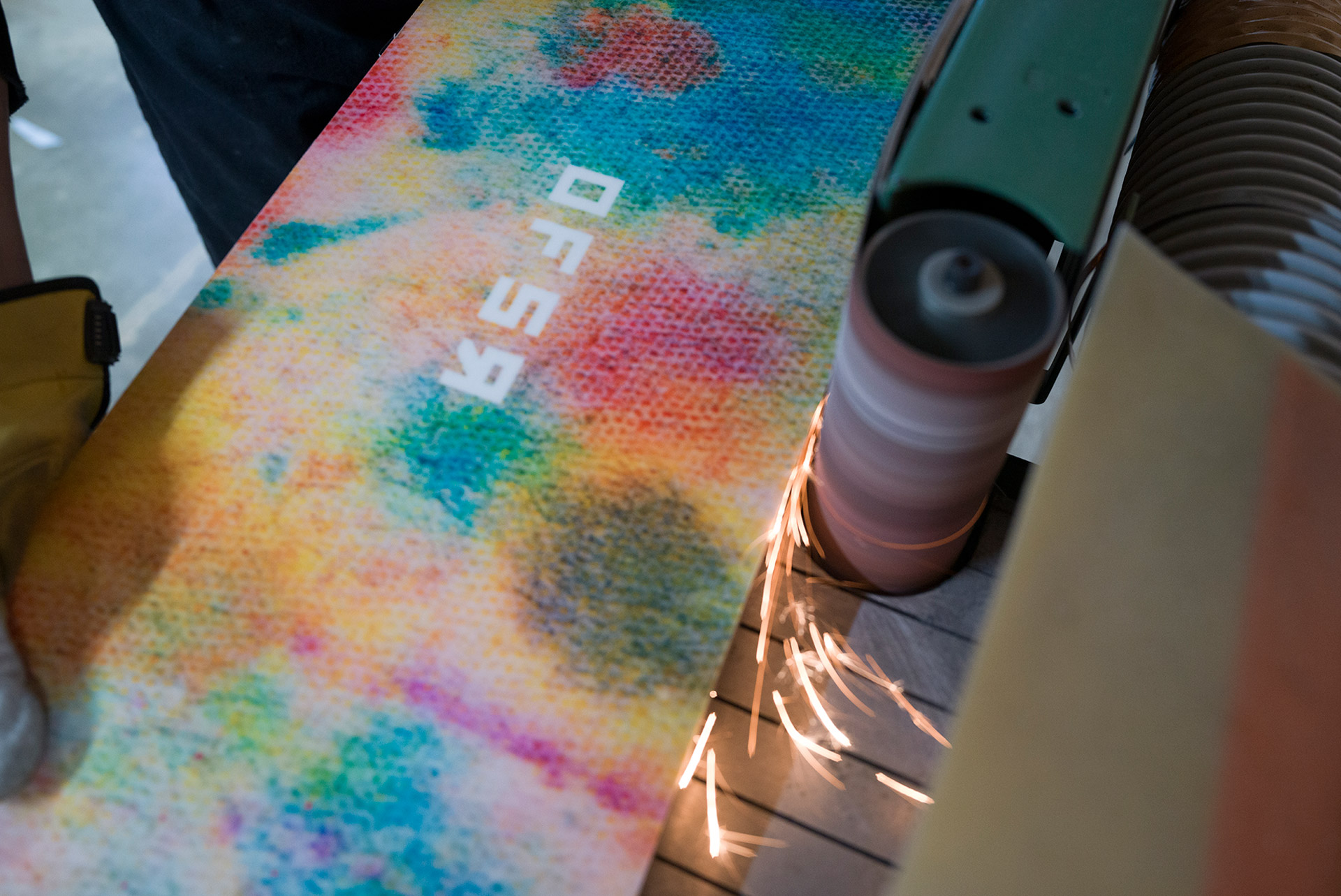 An iD board against the sander, sparks flying off the edge